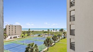 A view of a tennis court complex with a beach in the background.