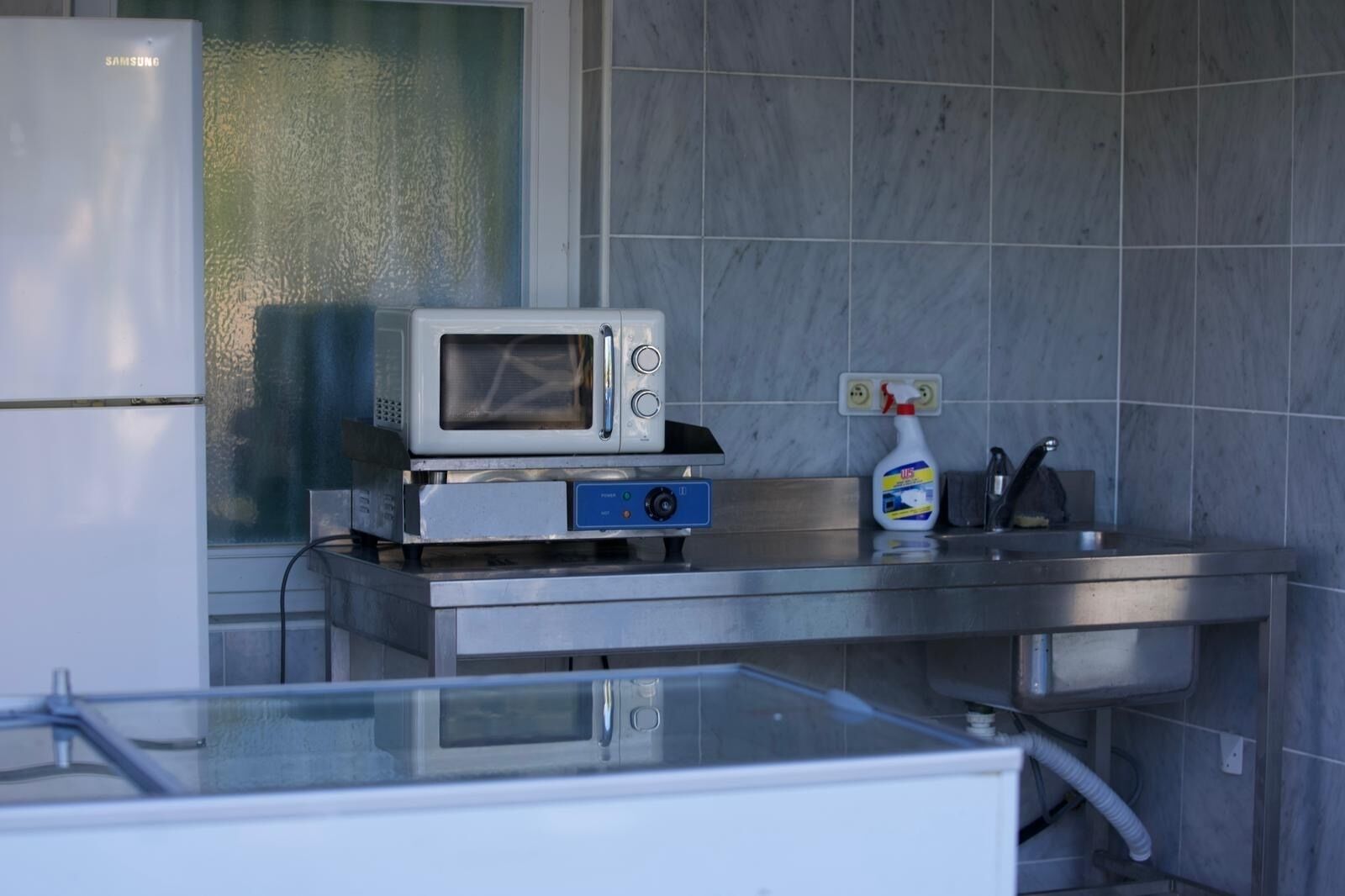 A compact kitchen with a microwave, a small sink, and a cleaning spray bottle.
