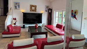Una sala de estar moderna con un televisor de pantalla plana grande, sofás rojo y blanco, una mesa de centro de vidrio y un jarrón decorativo.