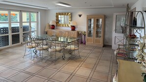 Un comedor con mesa de vidrio y sillas metálicas, un mueble con puertas de cristal y un espejo decorativo en la pared.