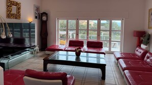 Un amplio salón con una gran mesa de centro de vidrio, sofás de cuero rojo, un televisor y vistas amplias a través de grandes ventanas.