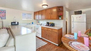 Cocina compacta con armarios de madera, un refrigerador blanco y una mesa de comedor con individuales rosa y azules.
