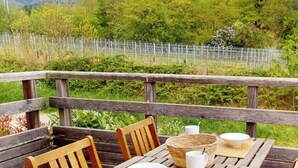 Una terraza de madera con una mesa y sillas, rodeada de vegetación y una valla.