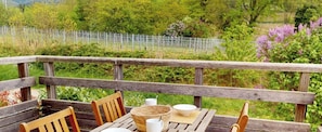 A wooden deck with a table and chairs, surrounded by greenery and a fence.