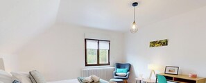 A bedroom with a bed, a chair, a desk, a radiator, a window, and a hanging light fixture.
