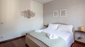 Ein ordentlich eingerichtetes Schlafzimmer mit Bett, Kissen, Nachttisch mit Lampe und Wandbildern.
