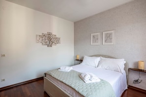 A neatly arranged bedroom with a bed, pillows, a bedside table with a lamp, and wall art.
