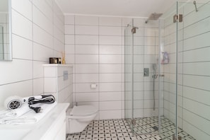A bathroom with a glass-enclosed shower, a white toilet, and a white sink with a towel and hairdryer. - Luxury 3 rooms Apt• Balcony• Parking | HaKerem A25 (Tel Aviv)