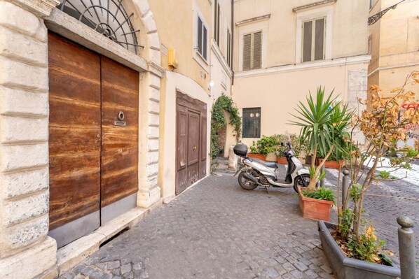 A narrow cobblestone street with a wooden door, a scooter, and potted plants.