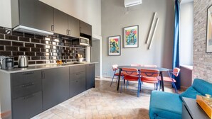 Een moderne keuken met grijze kastjes, een visgraatvloer en een eethoek met oranje stoelen en een blauwe bank.