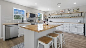 A modern kitchen with a central island, white cabinetry, and wooden countertops. - Rivers Oaks-The Ranch House Pool & Hot-Tub! (Fredericksburg)
