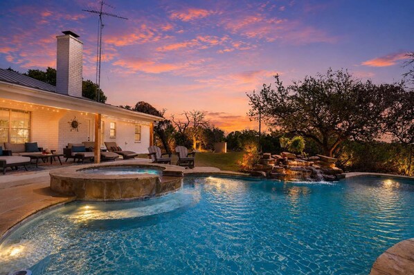 A swimming pool with a waterfall feature, surrounded by lounge chairs and a covered patio area.