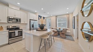 A modern kitchen with white cabinets, stainless steel appliances, and a central island with bar stools. - New! Waterside Lakewood Ranch, Tennis, Pool, Walk to Restaurants and More! (Sarasota)