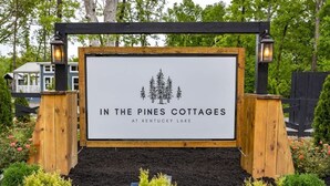 Schild für 'In the Pines Cottages' am Kentucky Lake, umgeben von angelegten Blumenbeeten und einem Holzzaun.