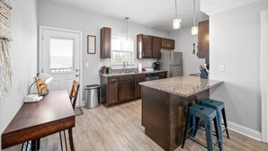 A modern kitchen with dark wood cabinets, a granite countertop island, and blue bar stools. - Unit #606 Summary:<br>19 (Clarksville)