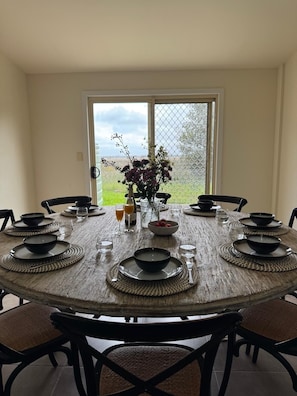 Une table de salle à manger ronde, avec des assiettes noires, des sets de table en fibres tressées et un vase rempli de fleurs.