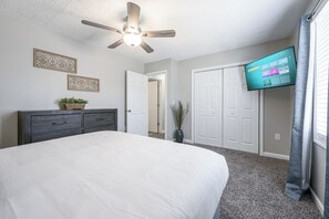 Une chambre à coucher avec un lit, une commode, un ventilateur de plafond, un téléviseur et une porte.