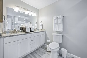 Une salle de bain moderne avec un grand miroir, des meubles blancs, des toilettes et un lavabo équipé d’un porte-serviettes.