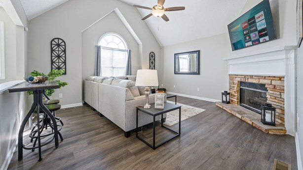 A living room with a high ceiling, a fireplace, a sofa, a coffee table, and a TV mounted on the wall.