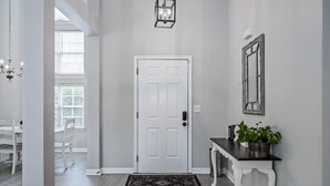 Un couloir avec une porte blanche, un tapis noir, une console blanche ornée d’une plante et un luminaire fixé au mur.