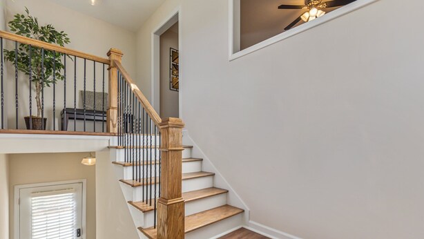 A staircase with wooden steps and black balusters, leading to a landing with a ceiling fan and a potted plant. - 27 West Ridge Drive SE, Cartersville (Cartersville)