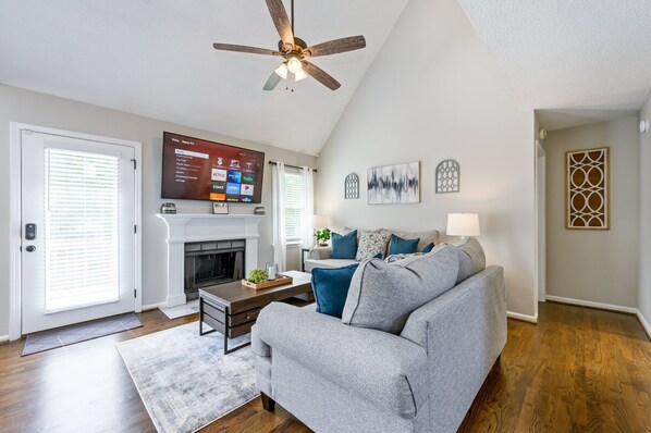 A living room with a gray sofa, a fireplace, a ceiling fan, and a mounted TV displaying a streaming service interface. - 13 Windfield Dr, Cartersville (Cartersville)