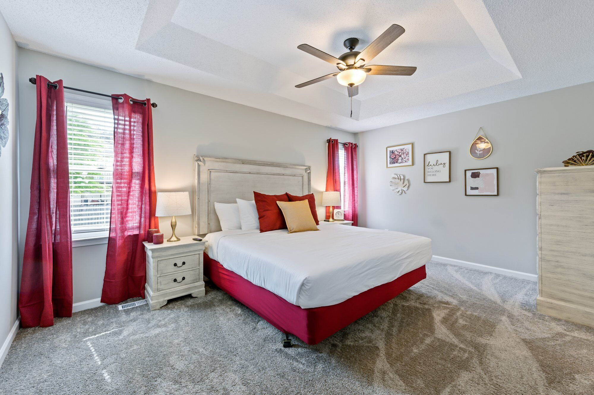 A bedroom with a bed, a nightstand, a ceiling fan, and a window with curtains.