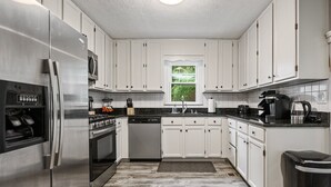 A modern kitchen with white cabinets, stainless steel appliances, and a window with a view of greenery.