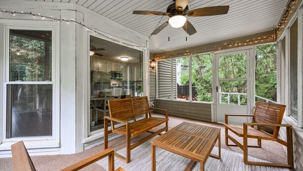 A covered patio with wooden furniture, a ceiling fan, and string lights.