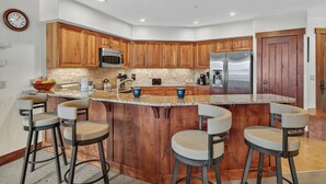 A modern kitchen with wooden cabinets, stainless steel appliances, and a central island with bar stools. - Ski-in/Ski-Out Retreat | Crystal Peak Lodge #7407 (Breckenridge)