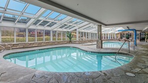Une piscine intérieure dotée d’un plafond en verre transparent, d’un sol en pierre et offrant une vue sur l’extérieur.