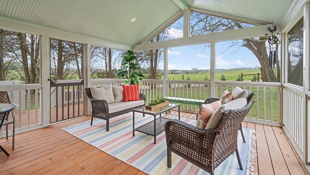 A covered porch with wicker furniture, a ceiling fan, and a view of a green field.
