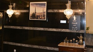 A lobby with a marble wall, a framed picture, a sign, and a small table with items. - فندق مرسى القصر Marsa Alqaser Hotel (Madinah)