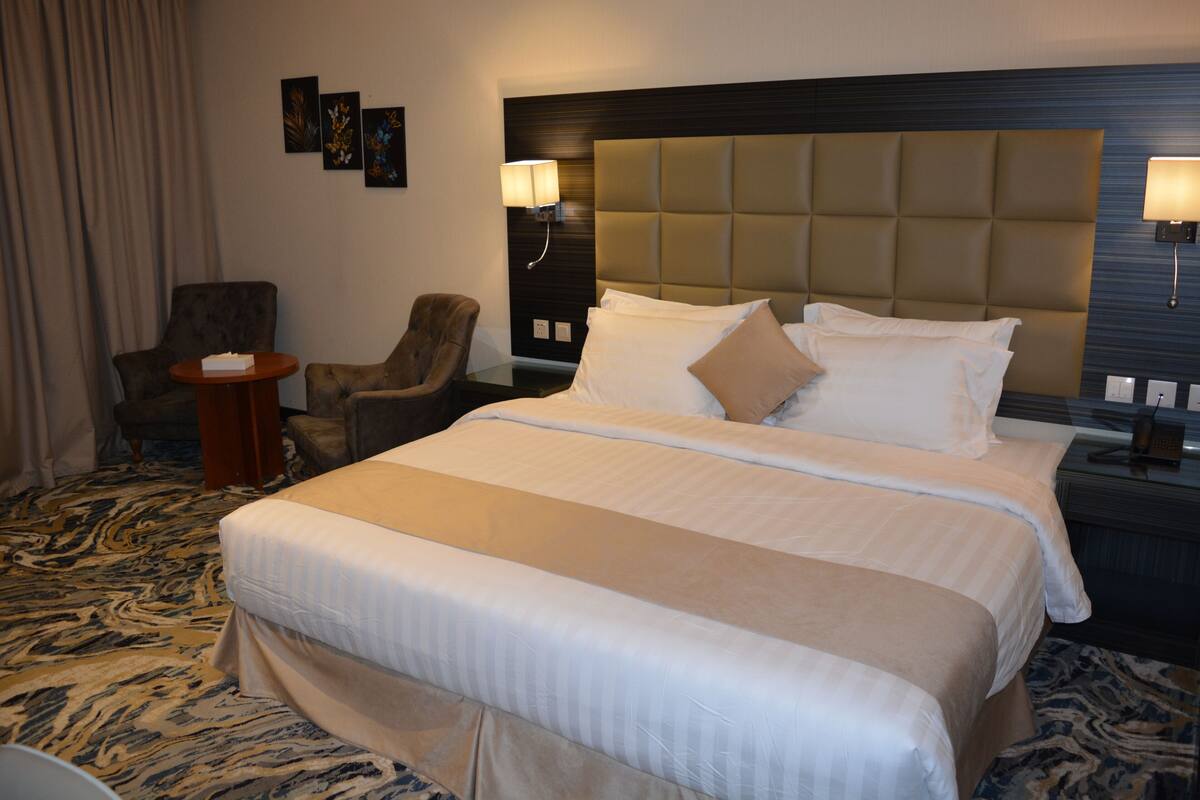 A hotel room with a large bed, two bedside tables, a chair, and a small round table.
