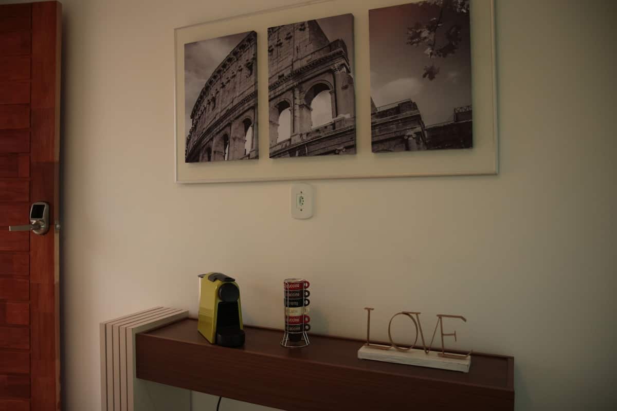 A wall with three framed pictures of the Colosseum, a coffee machine, a mug holder, and a 'LOVE' sign on a wooden shelf.
