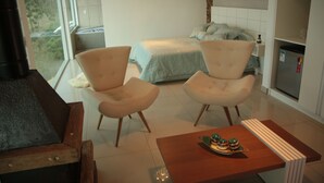 A modern hotel room with two plush armchairs, a wooden coffee table, a bed with a light blue bedspread, and a kitchen area with a refrigerator. - Unique Alta Vista Pousada Boutique (Córrego do Bom Jesus)