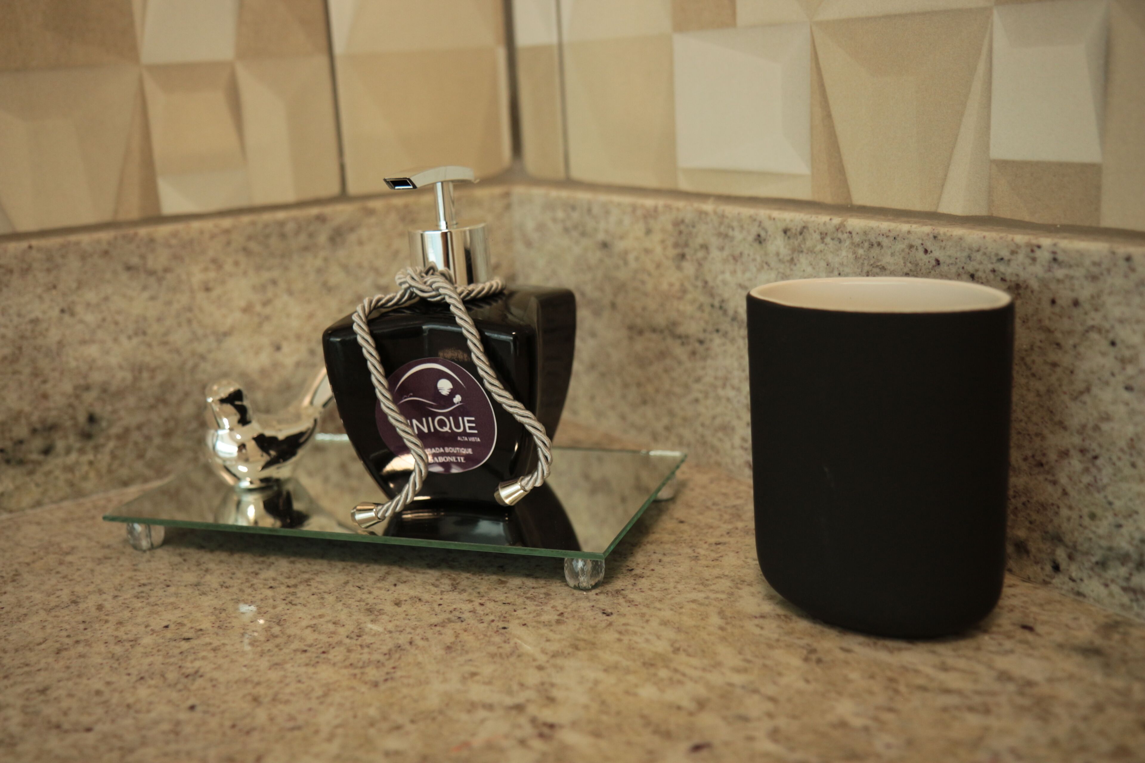 A bathroom counter with a glass soap dispenser and a black candle holder.