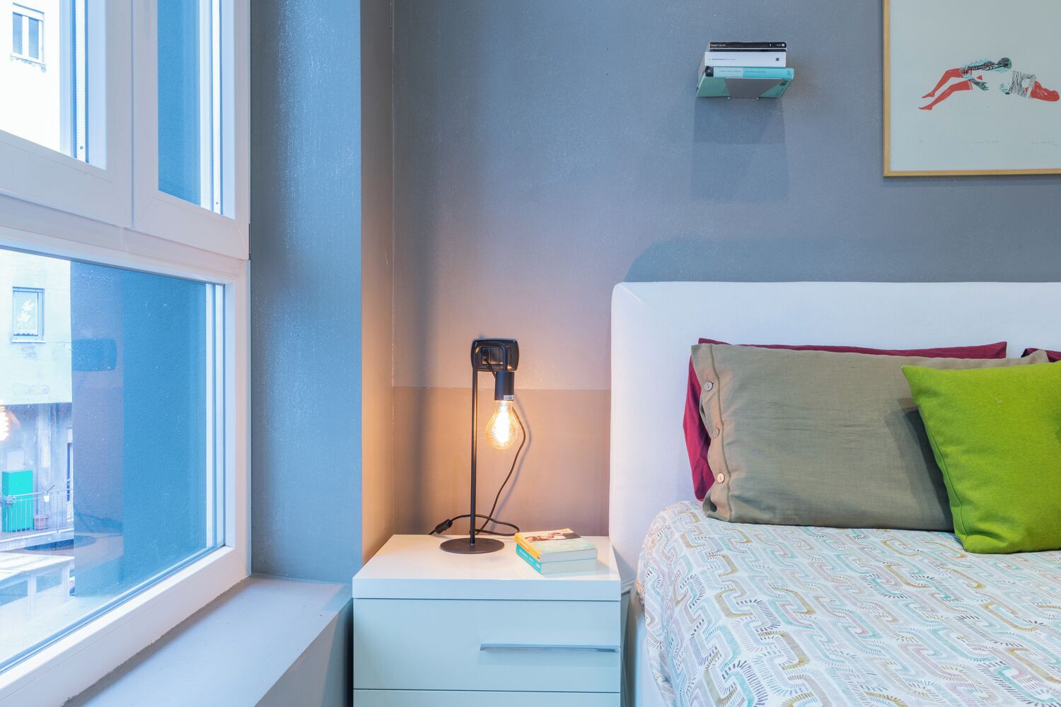 Une chambre à coucher comprenant un lit, une table de chevet avec une lampe, une fenêtre et un climatiseur fixé au mur.