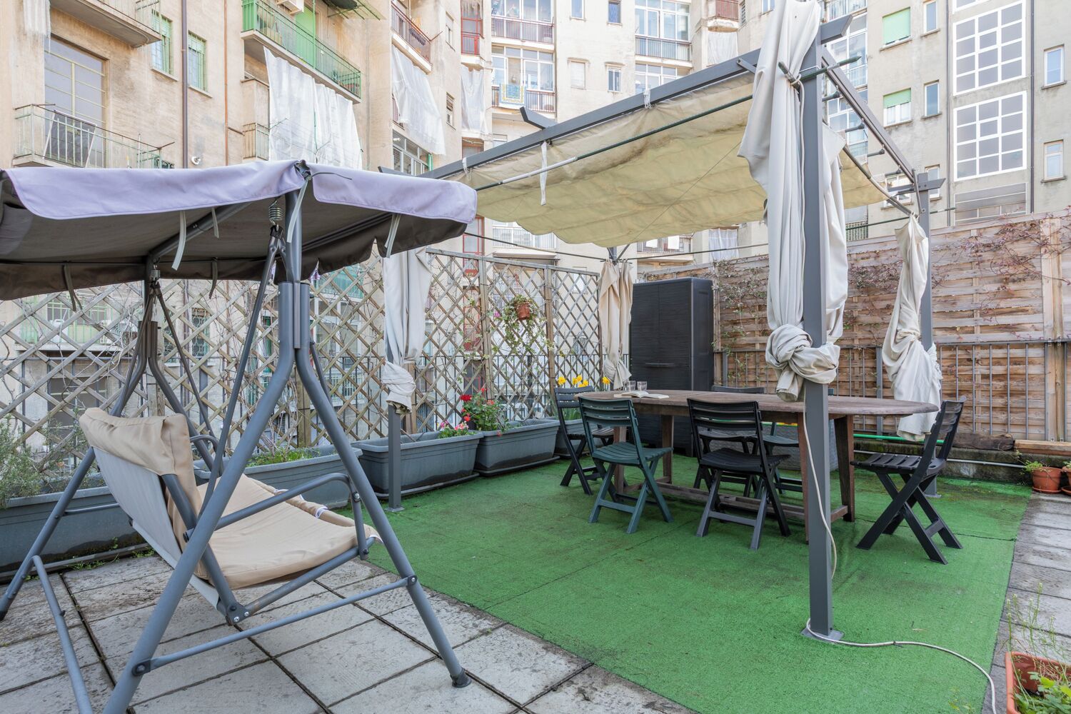 Une terrasse avec un fauteuil suspendu, une table avec des chaises et un téléviseur.