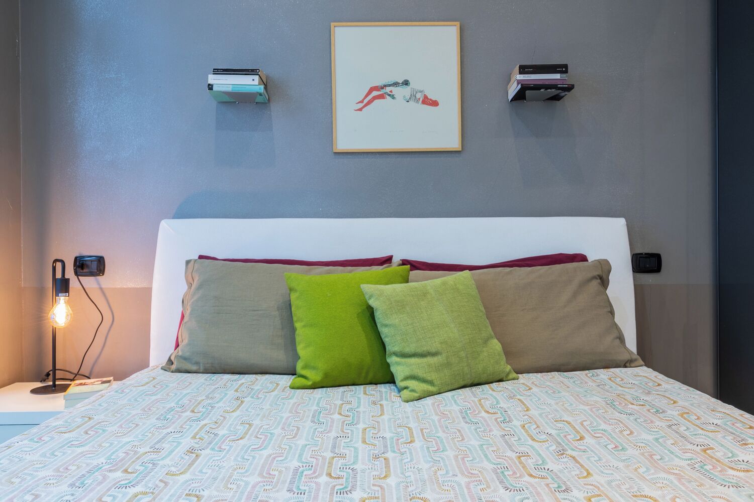 A neatly made bed with patterned bedding, a bedside lamp, and a framed artwork on the wall.