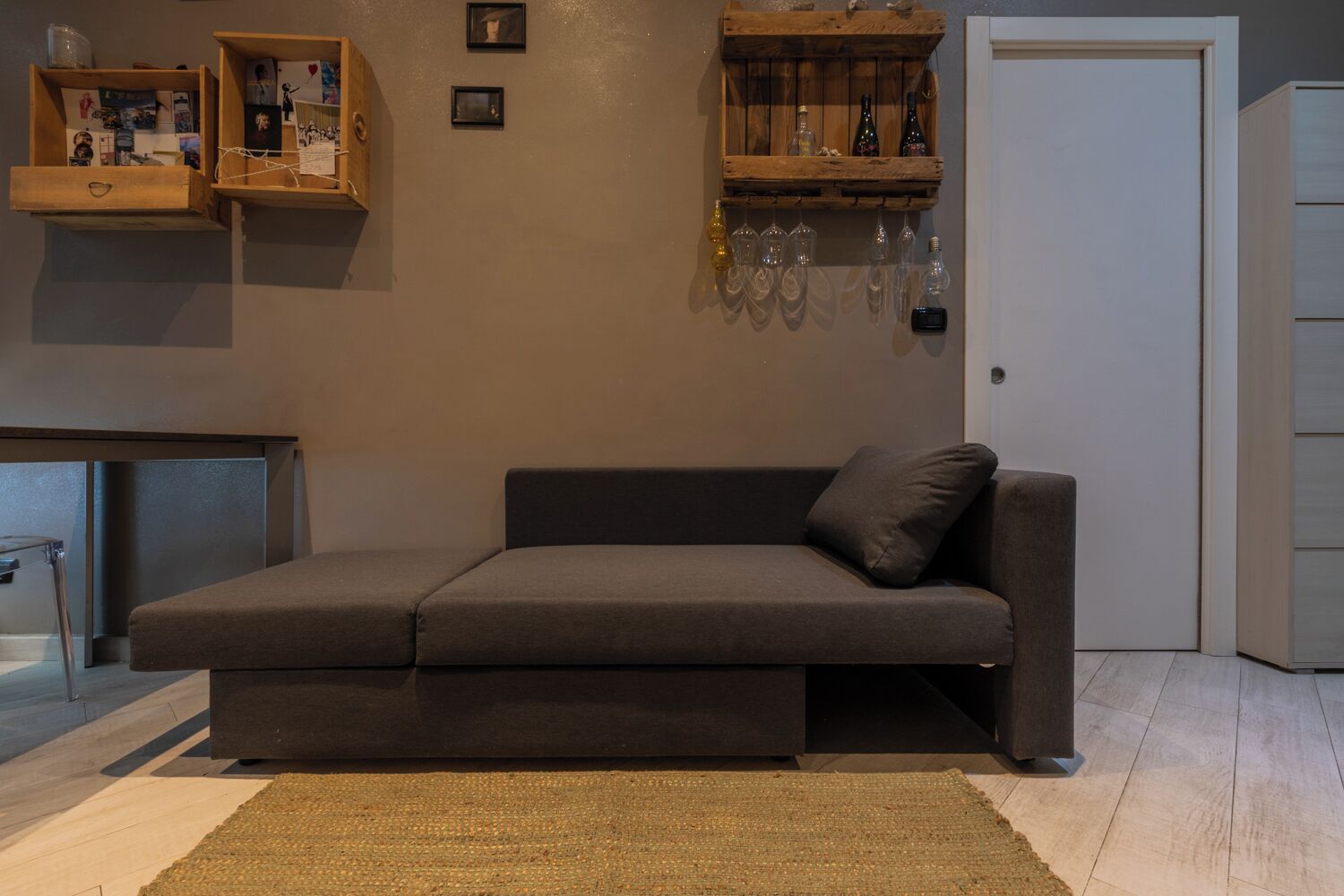 Un salon moderne comprenant un canapé, une table basse, une petite étagère en bois avec des photos et une porte.