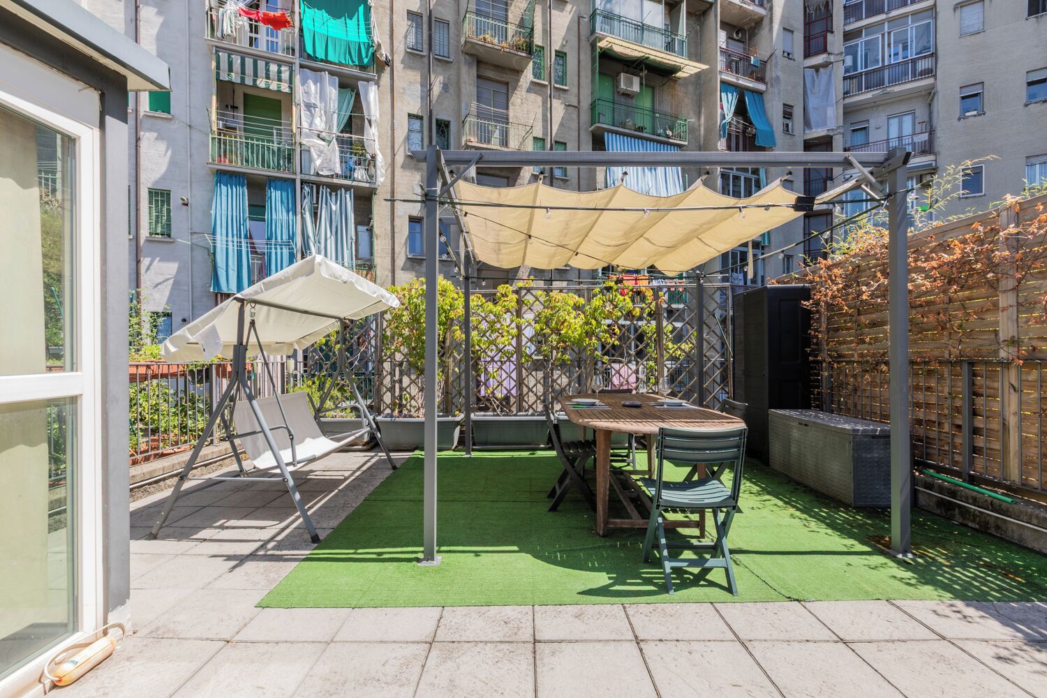 Eine Terrassengruppe im Freien mit Tisch, Stühlen, einer Schaukel und einem Pergola mit Dach.