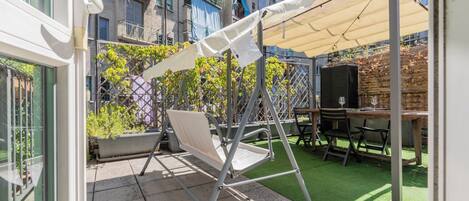 An outdoor patio with a swing set, a table with chairs, and a green artificial turf area.