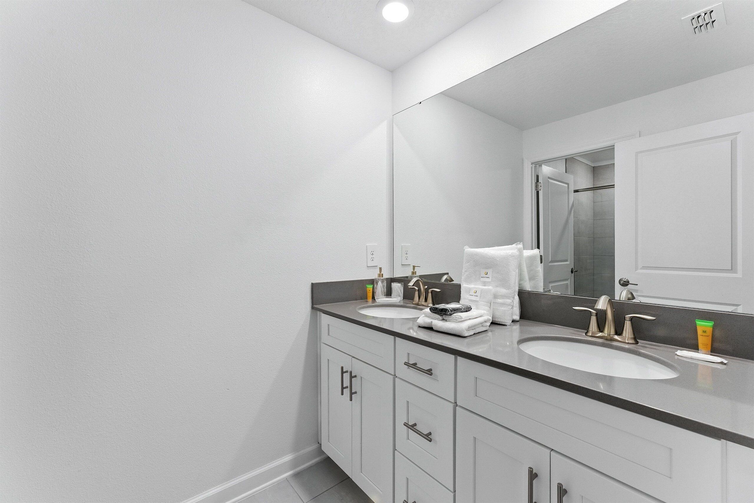 A modern bathroom with two sinks, a large mirror, and a walk-in shower.