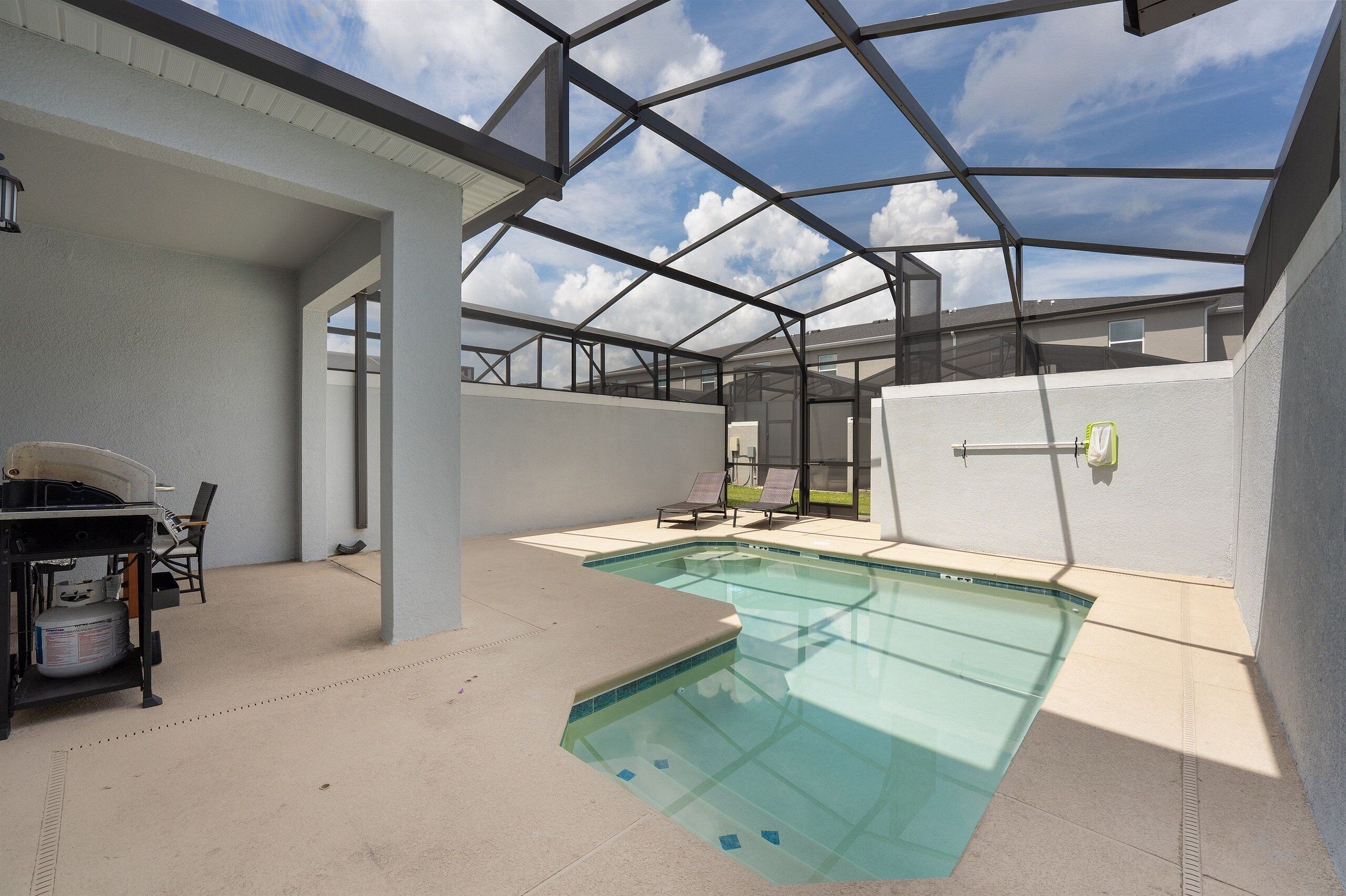 A covered outdoor swimming pool with a glass ceiling, a barbecue area, and lounge chairs.