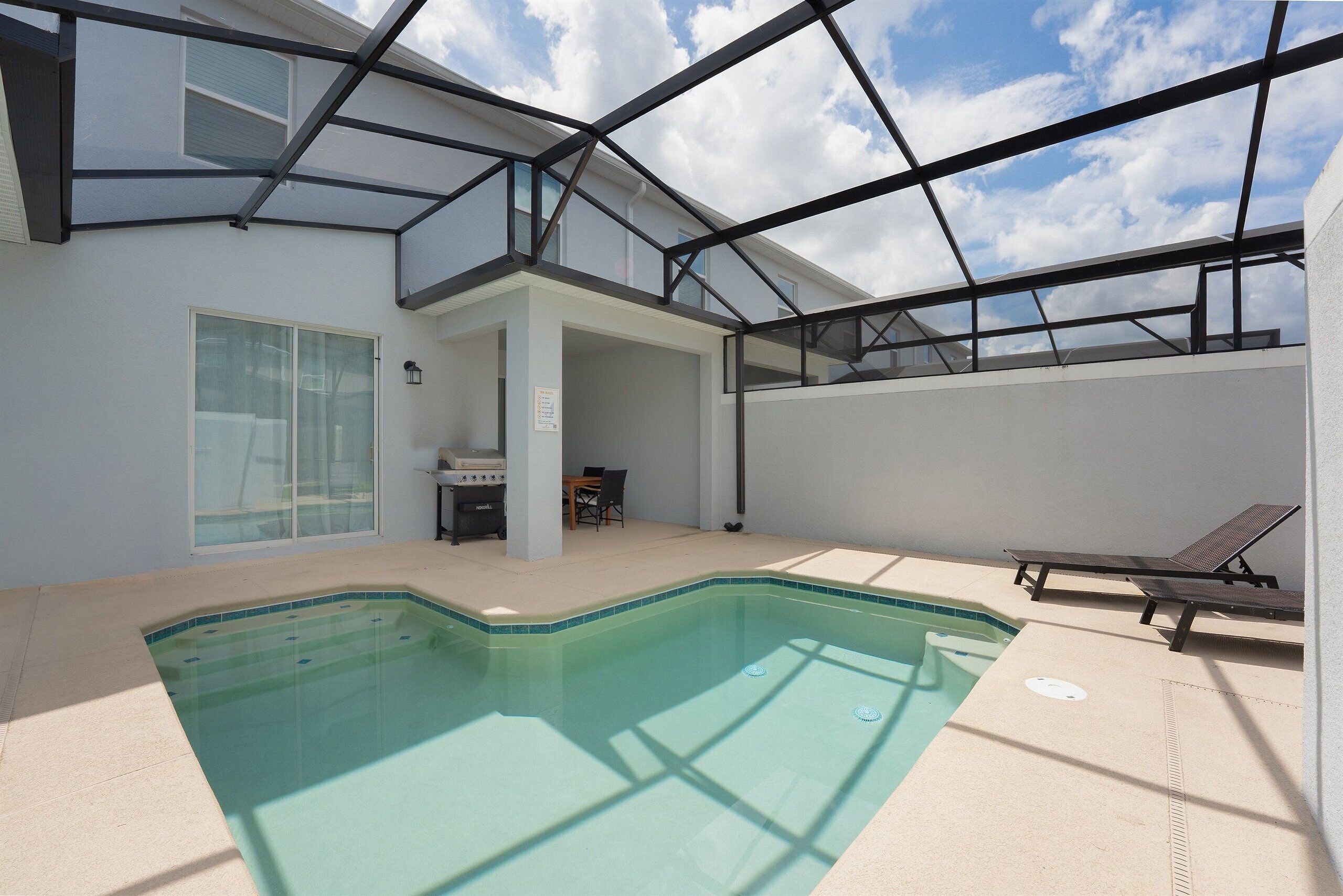 An indoor swimming pool with a glass ceiling, a lounge area with chairs, and a view of the sky.
