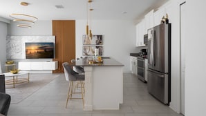 A modern kitchen with a central island, stainless steel appliances, and a dining area with a marble backsplash and a large painting. - Storey Lake Resort 4BR Home w/ Private Pool (Kissimmee)