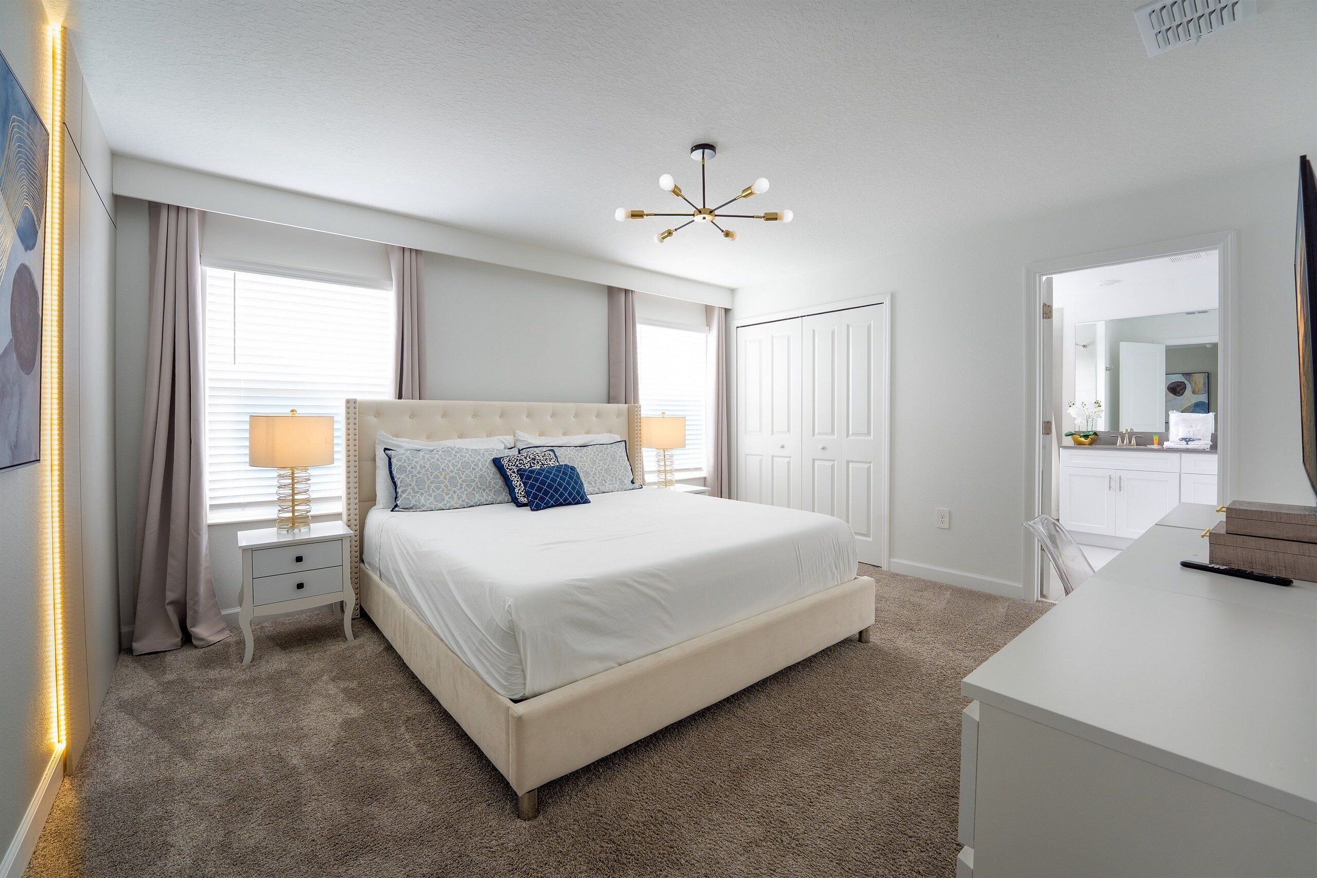 A bedroom with a large bed, bedside lamps, a ceiling light, and a view of the bathroom through an open door.