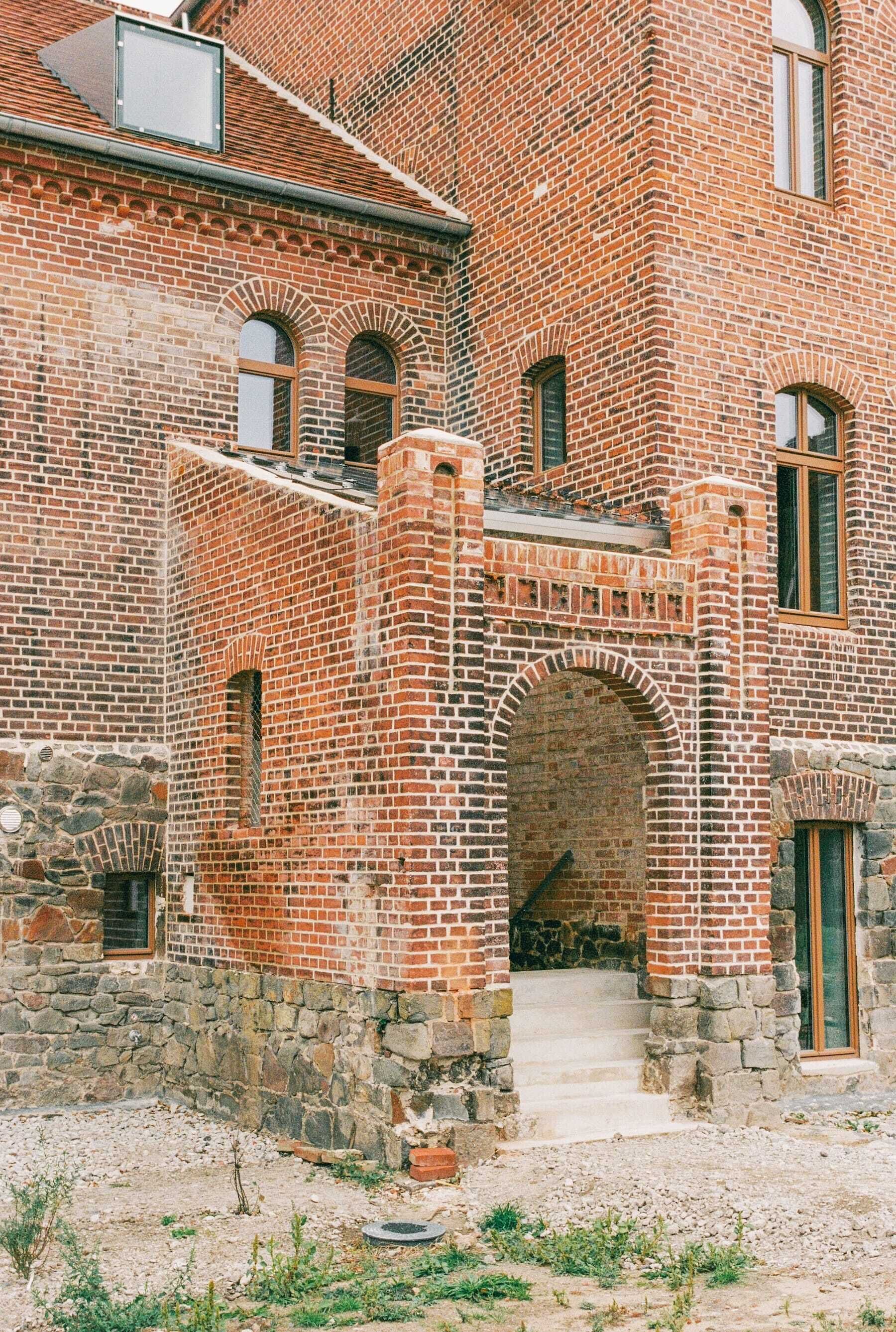 Un edificio histórico de ladrillo con base de piedra, puertas en arco y una escalera que conduce a un nivel superior.