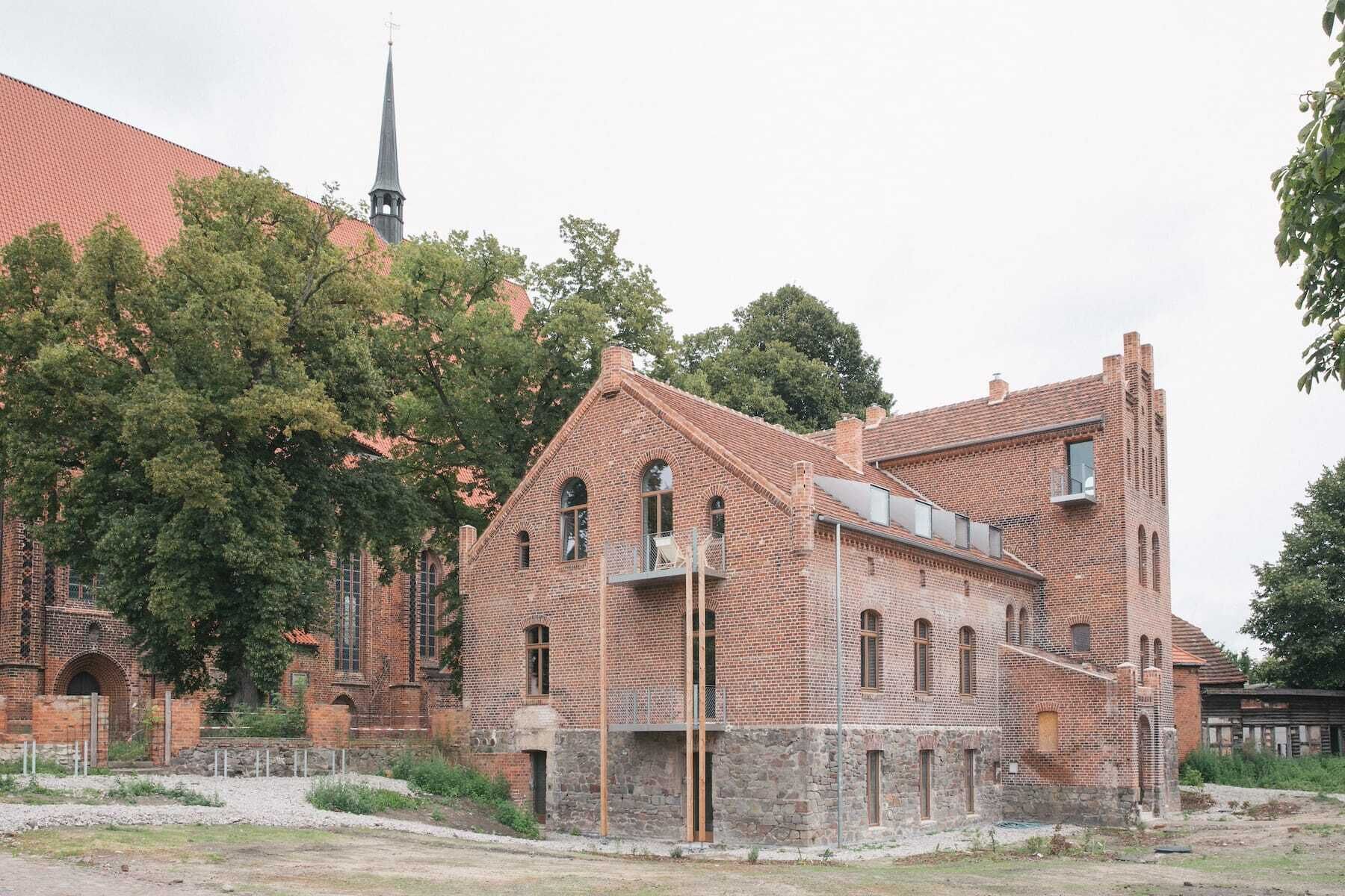 Un bâtiment historique en briques, doté d’un toit à forte pente, de grandes fenêtres et de fondations en pierre.